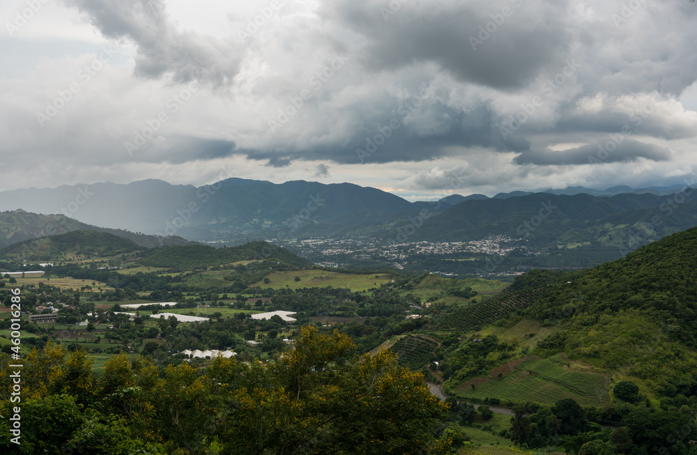 Dramatic image of approaching rainstorm in the valley of a Caribbean mountain town with fading hills and cloudy skies.
