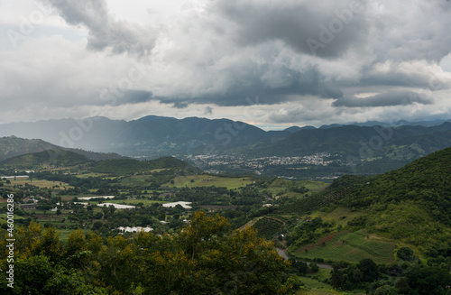 Dramatic image of approaching rainstorm in the valley of a Caribbean mountain town with fading hills and cloudy skies.