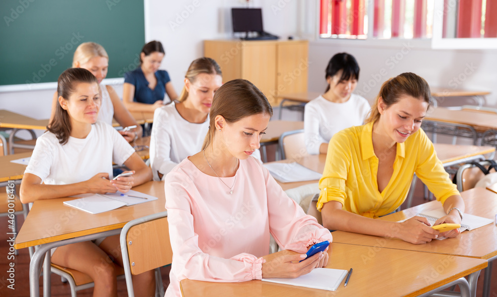 Multiracial female group of students using smartphones in classroom at university