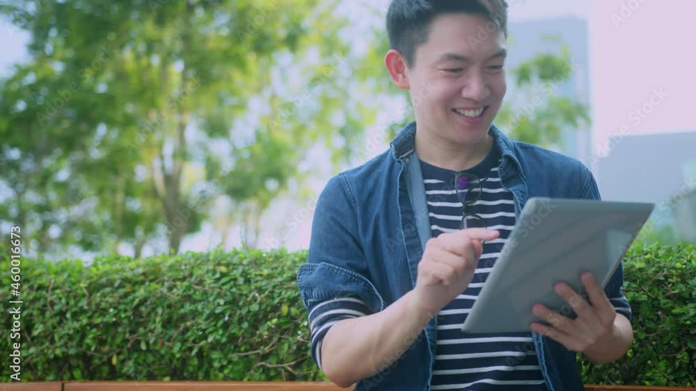 attractive asain male wearing glasses hand use tablet device playing game online relax leisure after work in outdoor garden technology ideas concept attractive asain male wearing glasses hand use tablet device playing game online relax leisure after work in outdoor garden technology ideas concept