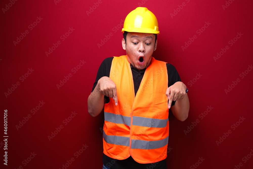 Wow Young asian man worker is surprised and shouting with pointing bottom with his hand on red background.
