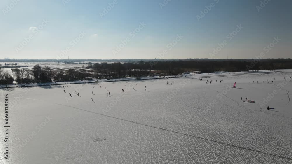 Aerial shot of beautiful snowy landscape with playing people on frozen lake during sunlight in Netherlands Aerial shot of beautiful snowy landscape with playing people on frozen lake during sunlight in Netherlands