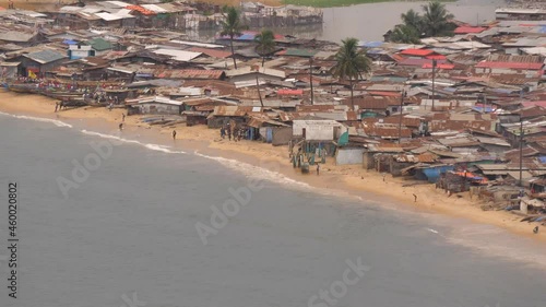People, boats, and shacks on West Point beach in Liberia, Monrovia next to Atlantic Ocean - telephoto from far photo