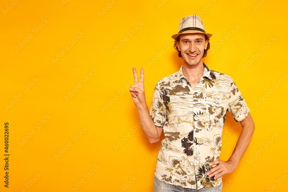 happy smiling male tourist traveler on vacation shows victory sign V, peace with his fingers on his hand. isolated yellow background with space for text. concept - people, adventures, flights abroad