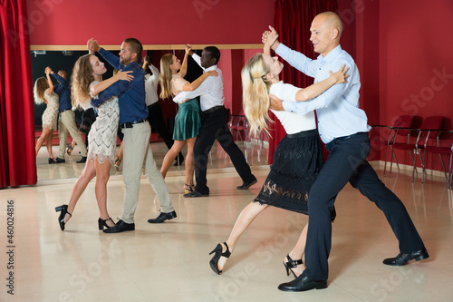 Adult dancing couples enjoying foxtrot in dance studio..