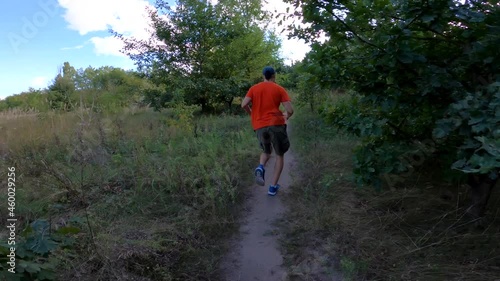 A man in a bright T-shirt runs uphill along a forest path. View from the back. Fitness concept.
