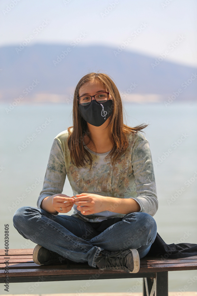 girl smiling and sitting on the beach, with protective mask due to covid-19, with musical note treble clef symbol