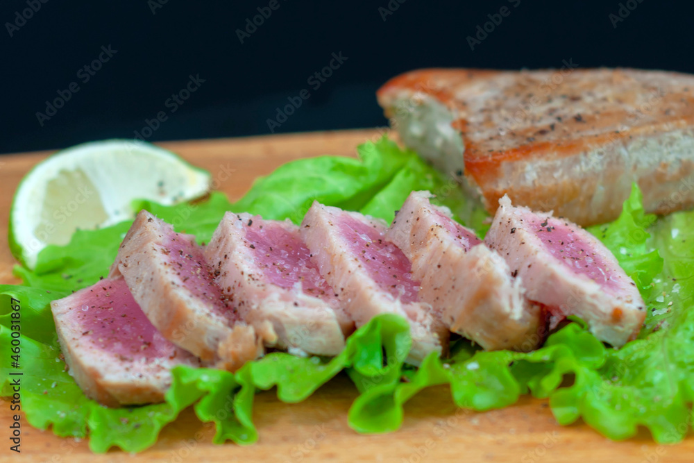 fried tuna steak cut into pieces lies on a wooden board on a black background. The concept of a healthy diet, a source of protein, useful trace elements, vitamins and omega. close-up.