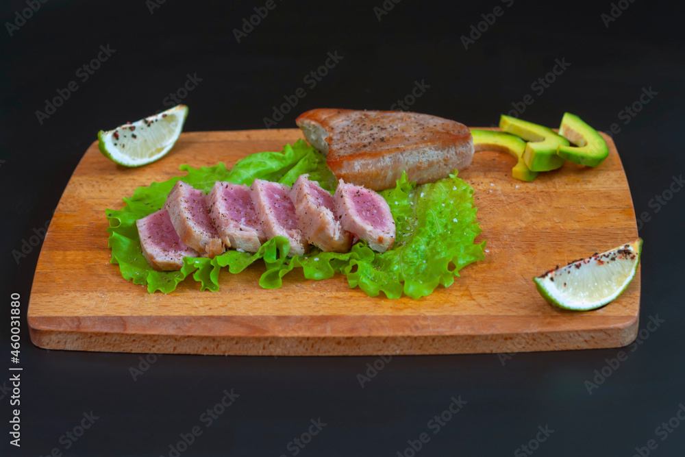 fried tuna steak cut into pieces lies on a wooden board on a black background. The concept of a healthy diet, a source of protein, useful trace elements, vitamins and omega. fried tuna steak cut into pieces lies on a wooden board on a black background. The concept of a healthy diet, a source of protein, useful trace elements, vitamins and omega.