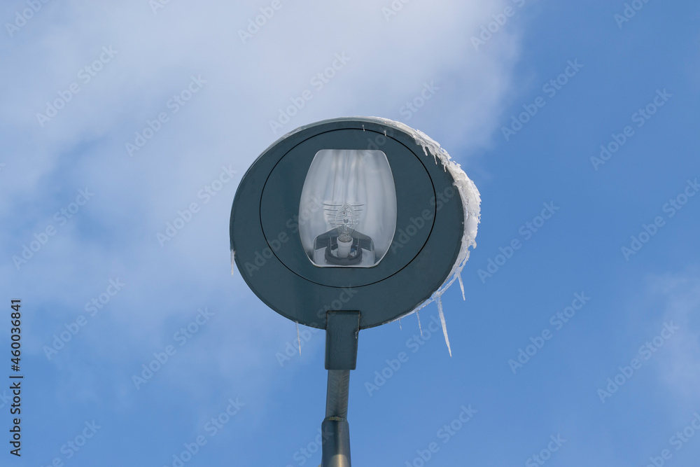 Street lamp covered with ice and icicles. Background - blue sky. Winter season concept.