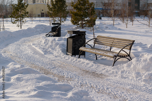 City square in winter. Snow-covered path, bench. Snowy white drifts. Winter season concept.