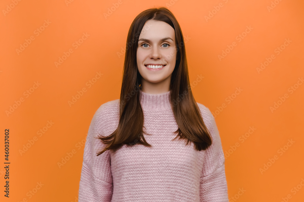 Portrait of cute young smiling positive friendly cheerful caucasian woman, happy looking camera, wearing pink knitted sweater, posing isolated over orange background studio. People lifestyle concept Portrait of cute young smiling positive friendly cheerful caucasian woman, happy looking camera, wearing pink knitted sweater, posing isolated over orange background studio. People lifestyle concept