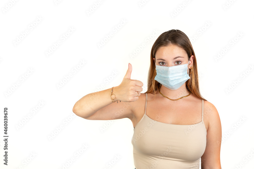 Young woman with face mask and thumb up. 20 - 22 years old. Isolated on white background. White European Woman. Young woman with face mask and thumb up. 20 - 22 years old. Isolated on white background. White European Woman.