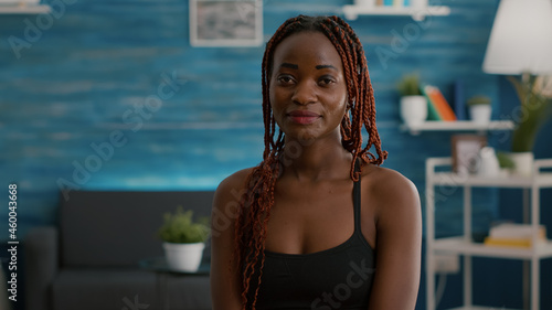 Portrait of athlete with black skin looking into camera while siting on aerobics ball during morning workout in living room. Strong adult practicing gymnastics warming before aerobics photo