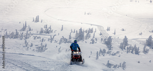 a snowmobiler rides and jumps in the snowy mountains. prof pilot of a mountain snowmobile in bright gear without brands for travel advertising