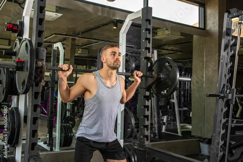 young man with barbell flexing muscles and making shoulder press squat in gym