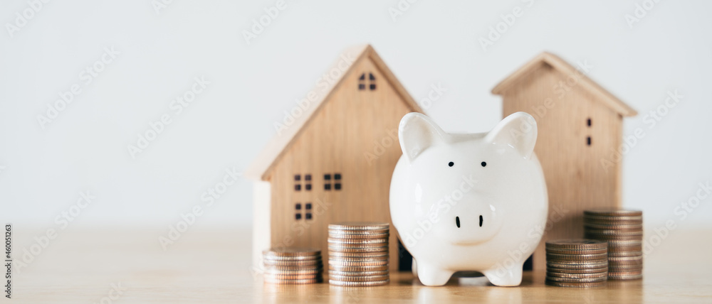 Wooden house with white piggy bank and stacking coins on wooden table. saving money for buying house, financial plan home loan concept. - obrazy, fototapety, plakaty 