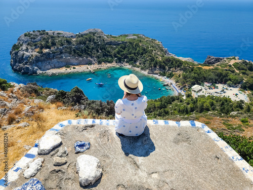 The girl in a straw hat looks from above at the Anthony Quinn Bay on Rhodes Island, Greece