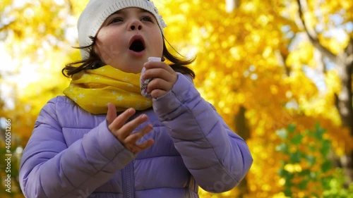 Autumn portrait of a girl 7 years old in the park. The child coughs into a handkerchief. Colds and viral diseases in cool weather. Place for your text.