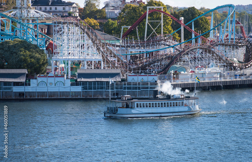 Old steam commuting boat from 1890s in front of an amusement park in Stockholm with rollercoasters and merry go rounds