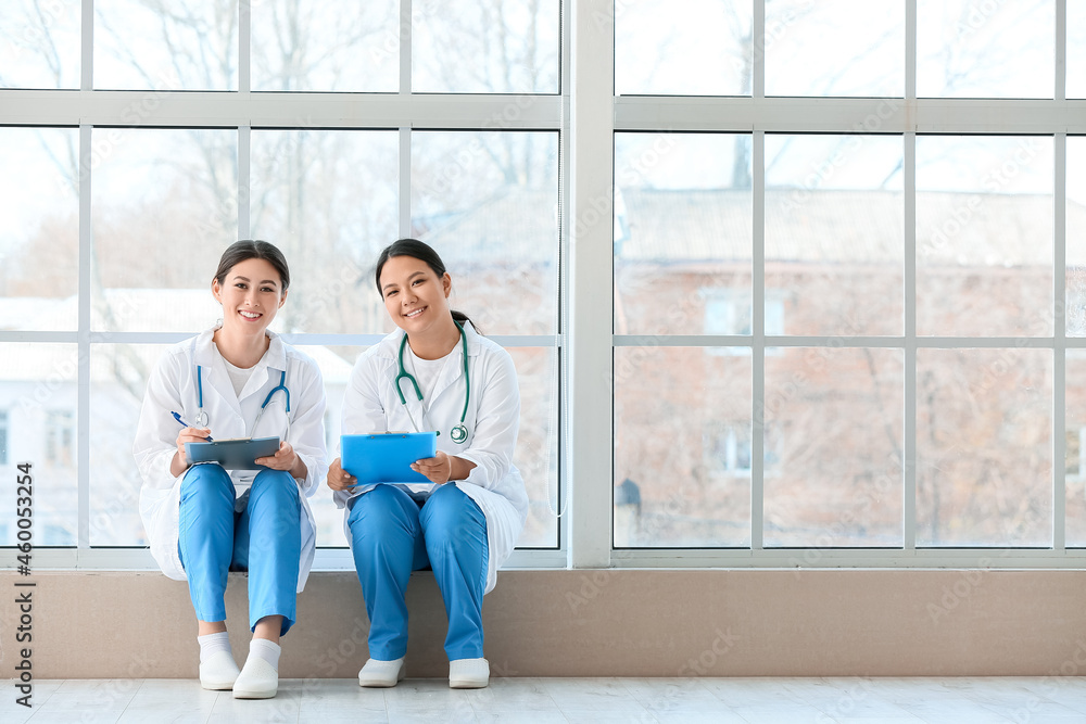 Female Asian doctors sitting on window sill in clinic Female Asian doctors sitting on window sill in clinic
