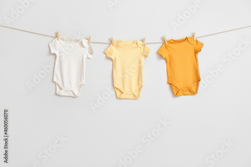 Stylish baby clothes hanging on rope against white background