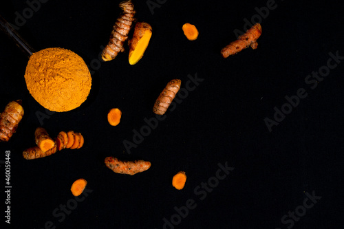 Turmeric (curcumin) powder in a wooden ladle and fresh rhizome on a black background, For spices and medicine.