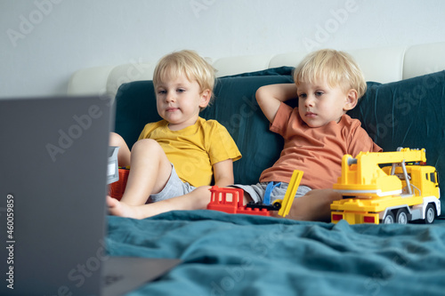 cute little caucasian kids boys twins using laptop in bed at home. Kids using technology