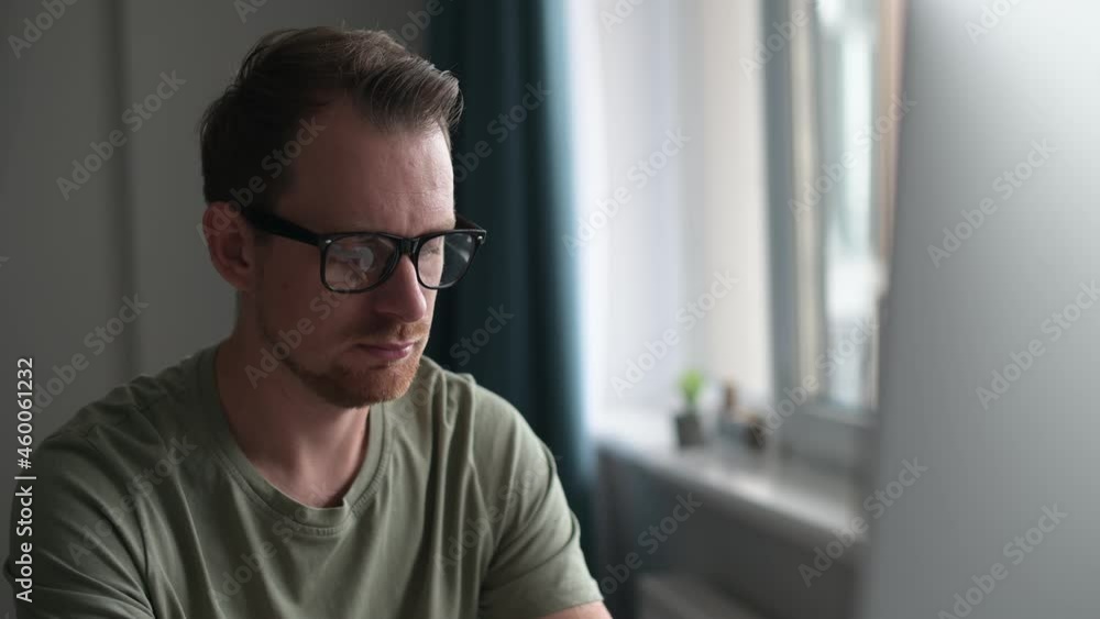 Concentrated young hipster freelancer man with beard in glasses sitting at the table and looking at the PC monitor, focused guy working from home, typing messages, answering emails Concentrated young hipster freelancer man with beard in glasses sitting at the table and looking at the PC monitor, focused guy working from home, typing messages, answering emails