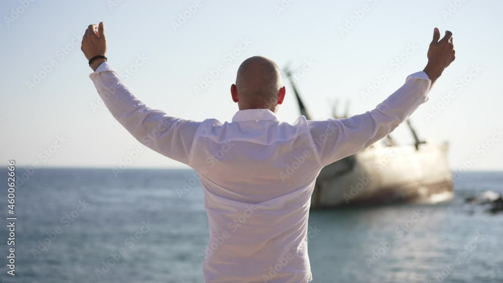 Back view of free Caucasian happy man stretching hands in slow motion admiring beauty of blue Mediterranean sea with sunken ship. Carefree confident male tourist enjoying leisure on sunny summer day Back view of free Caucasian happy man stretching hands in slow motion admiring beauty of blue Mediterranean sea with sunken ship. Carefree confident male tourist enjoying leisure on sunny summer day