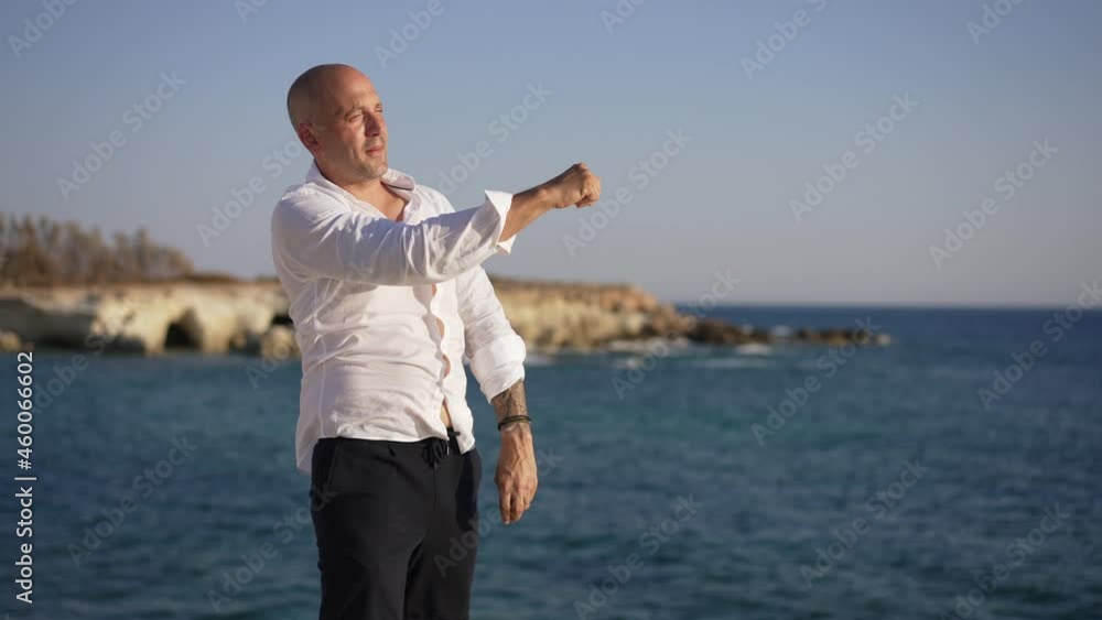 Side view confident man throwing stone in dark blue Mediterranean sea water in slow motion. Happy carefree Caucasian tourist smiling admiring beauty of landscape outdoors in sunshine Side view confident man throwing stone in dark blue Mediterranean sea water in slow motion. Happy carefree Caucasian tourist smiling admiring beauty of landscape outdoors in sunshine
