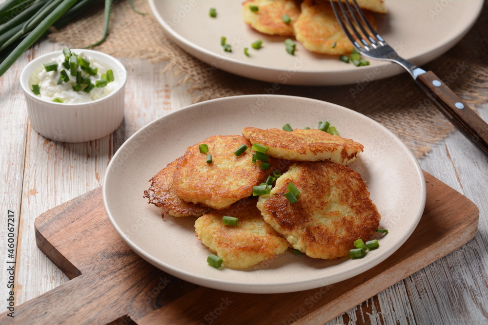 Potato pancakes or latkes or draniki with sour cream in plate on wooden table.