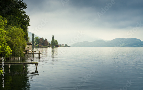 View of calm lake Zugersee with mountains in the background and cloudy sky, from the Swiss city of Zug. © csbphoto