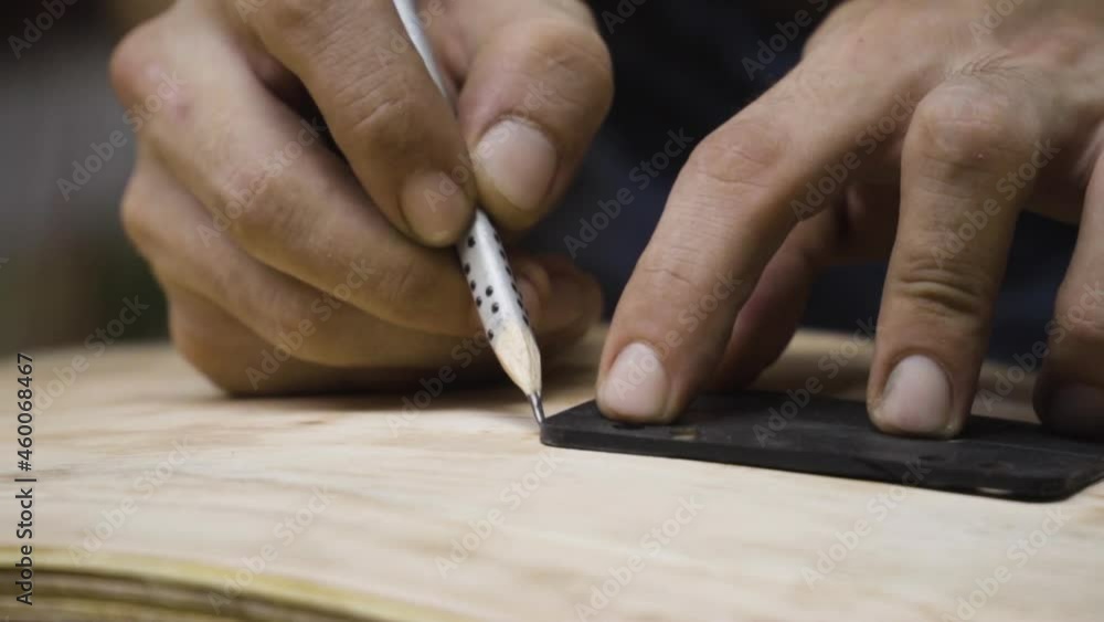 Hands of craftsman marking wheels location on skateboard with pencil, motion view Hands of craftsman marking wheels location on skateboard with pencil, motion view