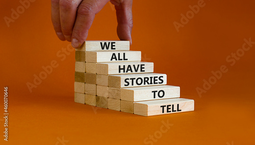 We all have stories to tell symbol. Wooden blocks with words 'We all have stories to tell'. Businessman hand. Beautiful orange background. Business, popular quotation concept. Copy space. photo