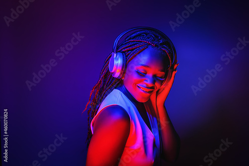 Stylish fashion african american teenager model wearing headphones listening dj music dancing in purple neon lights. Young teen girl enjoy cool music