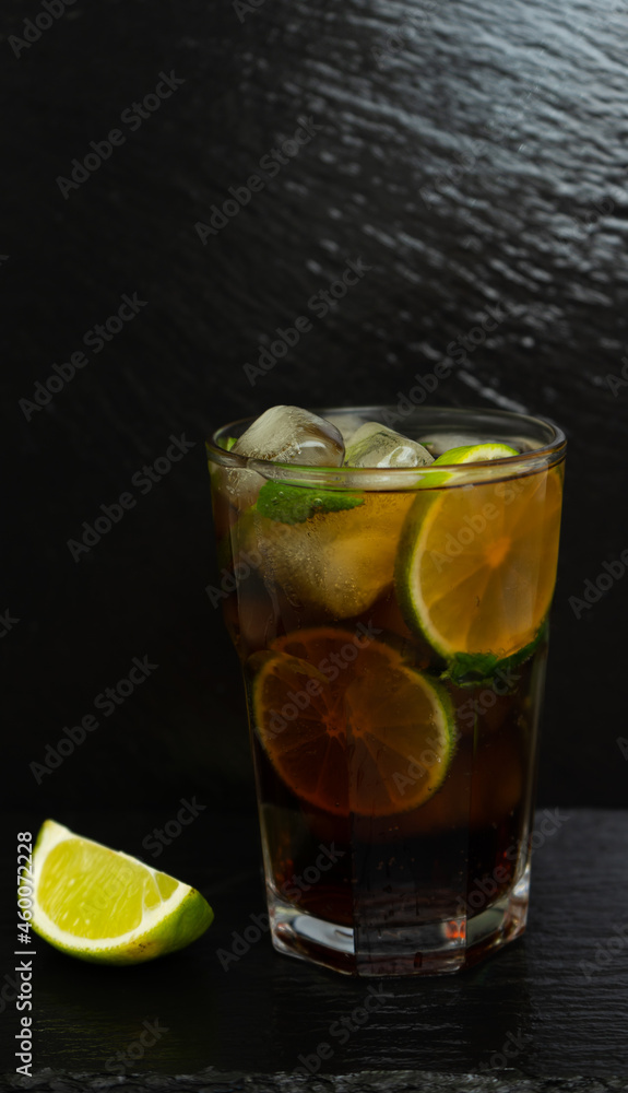Cuba Libre cocktail with brown rum, lemon juice, coke and ice cubes, decorated with fresh lime slice on modern black stone tray Cuba Libre cocktail with brown rum, lemon juice, coke and ice cubes, decorated with fresh lime slice on modern black stone tray