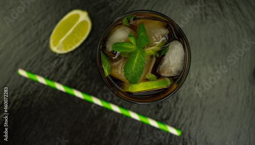 Cuba Libre cocktail with brown rum, lemon juice, coke and ice cubes, decorated with fresh lime slice on modern black stone tray