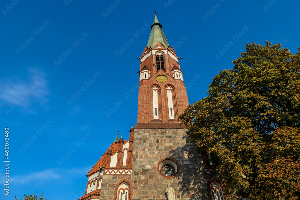 A close up of a bell tower of a church in Sopot, Poland. The church is surrounded by high, lush trees. The sky above is blue and cloudless. Spirituality.