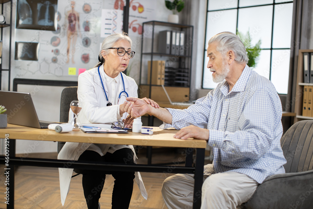 Senior female doctor holding fingers on wrist of male patient while checking pulse. Professional medical examination at modern clinic. Regular check up during retirement. Senior female doctor holding fingers on wrist of male patient while checking pulse. Professional medical examination at modern clinic. Regular check up during retirement.