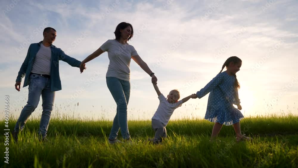 Happy family is walking on green grass.Family walk along rural road. Children with parents outdoors in park. Group of people are walking on grass in field. Happy family concept in park Happy family is walking on green grass.Family walk along rural road. Children with parents outdoors in park. Group of people are walking on grass in field. Happy family concept in park