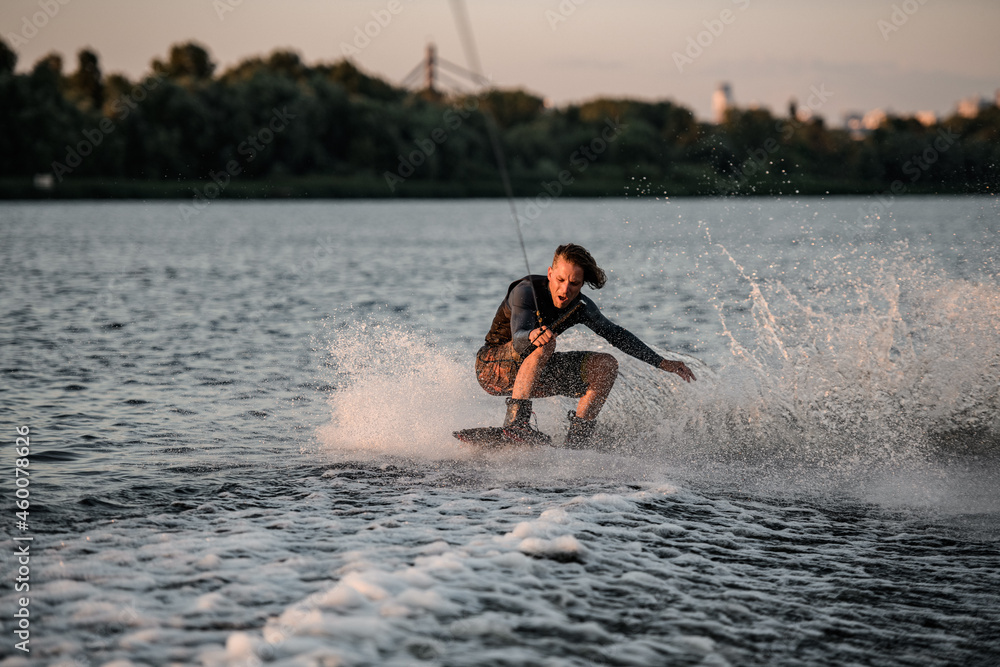 energetic man in wetsuit balancing on wakeboard and riding a splashing wave.