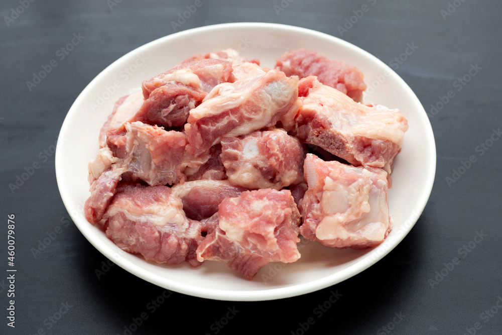 Raw pork ribs in white plate on dark background.