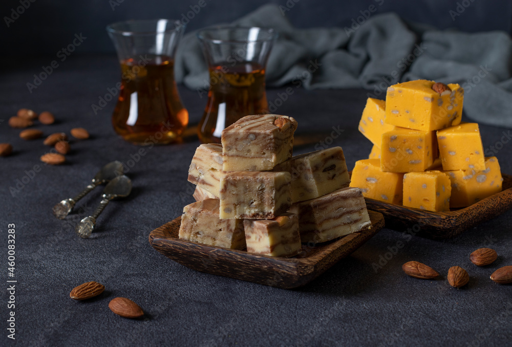 Traditional Uzbek sweet halva with almonds, cocoa, melon and sunflower seeds on an iron tray and two cups of tea on a dark background. Traditional Uzbek sweet halva with almonds, cocoa, melon and sunflower seeds on an iron tray and two cups of tea on a dark background.
