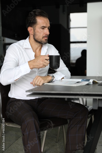 Poranna prasa i praca podczas pierwszej kawy. Przystojny mężczyzna w białej koszuli pije poranną kawę. 