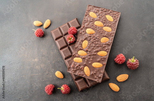 assortment chocolate bars with almonds, raspberries, handmade sweets. Composition of bars milk and dark almond chocolate, raspberries on a black background, top view. Pastry craft on the table