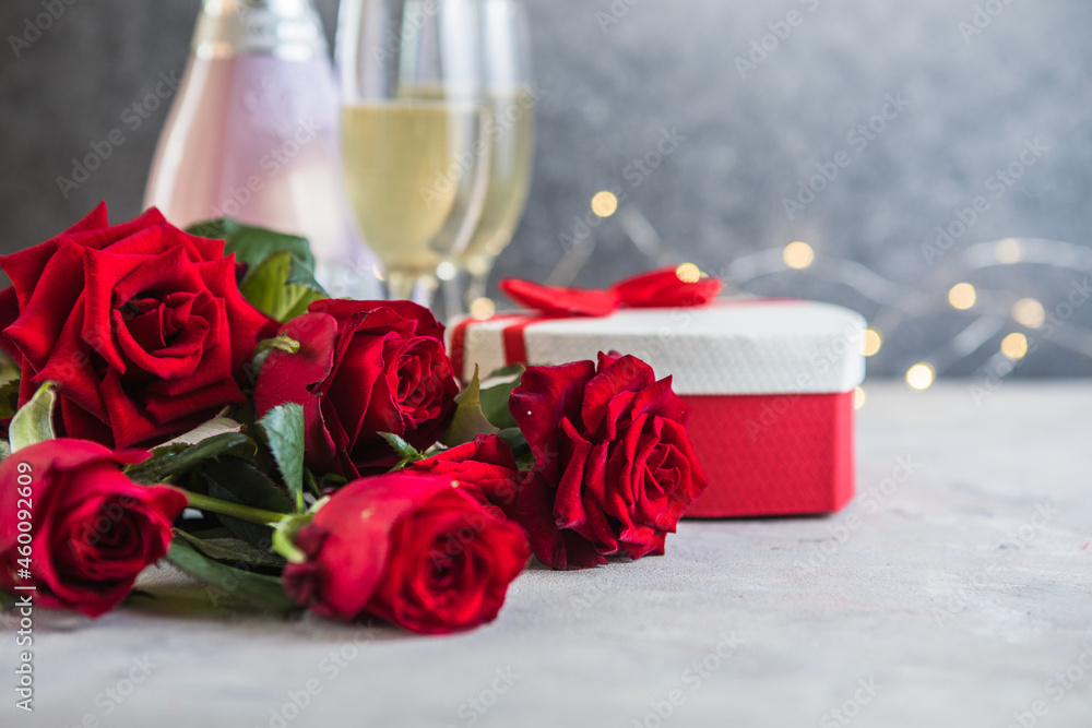 Champagne and red roses with bokeh. Valentine's setting with red roses and present