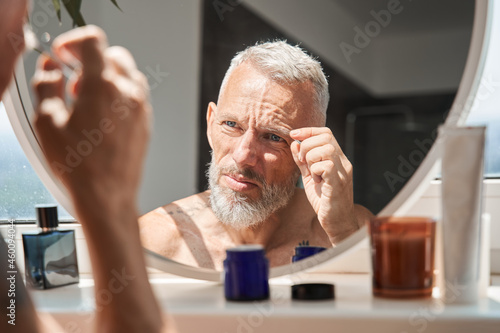 Mature man tweezing eyebrows on his face photo