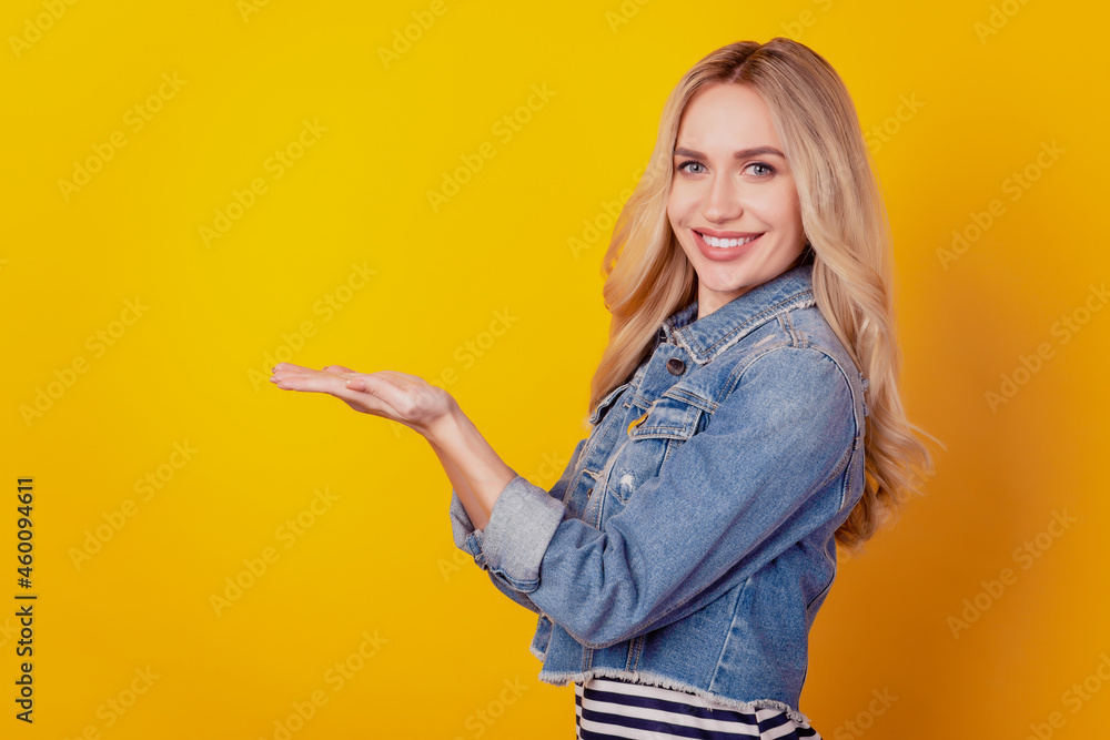 Portrait of cheerful lovely cute lady palm hold empty space shiny smile on yellow background