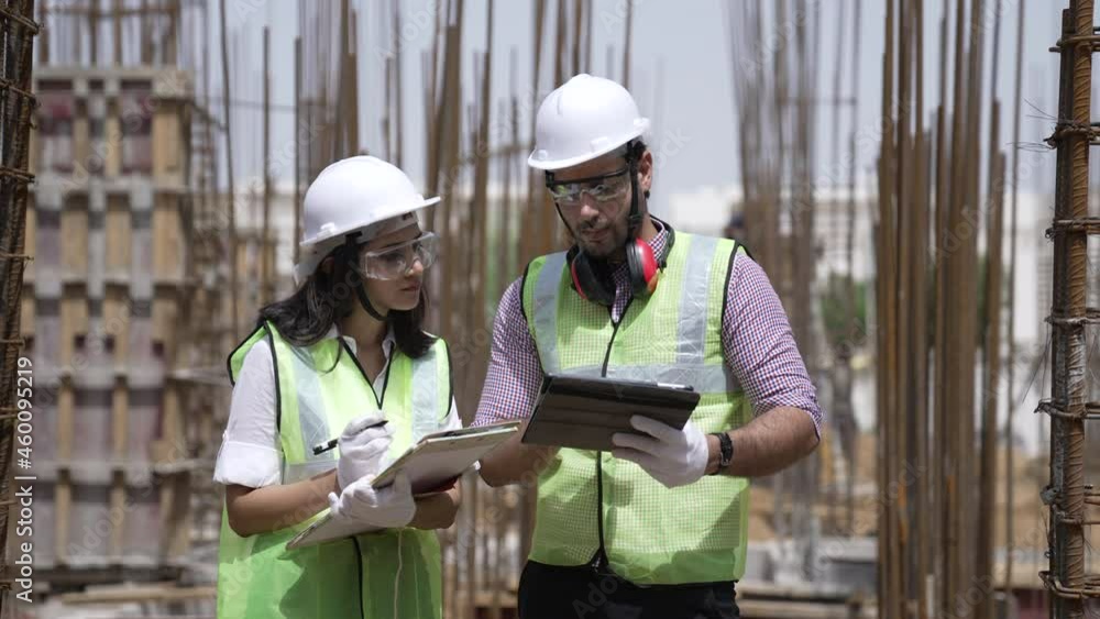 Two Indian engineers lady and man wearing safety helmets and face mask with eyeglass they have a discussing conversation together on construction site.Foreman and his assistant lady talking together. Two Indian engineers lady and man wearing safety helmets and face mask with eyeglass they have a discussing conversation together on construction site.Foreman and his assistant lady talking together.